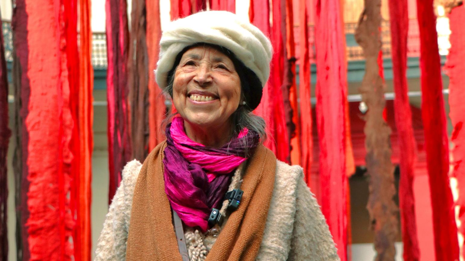 Fotografía de la artista Cecilia Vicuña junto a su instalación Quipu menstrual