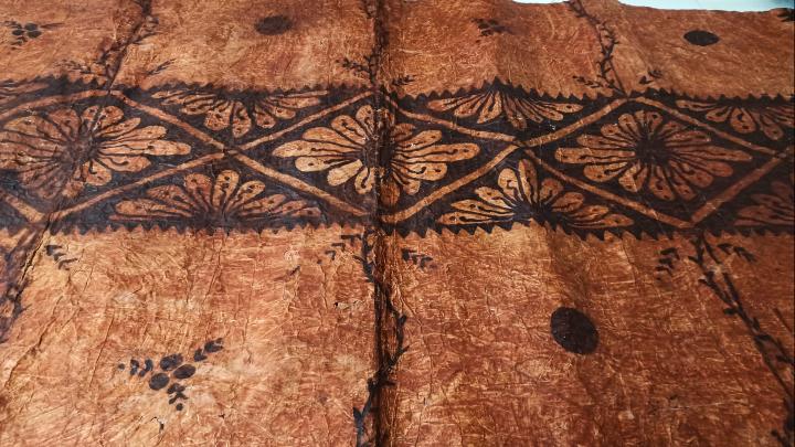 Tapa o pieza textil proveniente de Tonga, confeccionada por las fibras de mahute, con diseños de tonalidades cafés. 